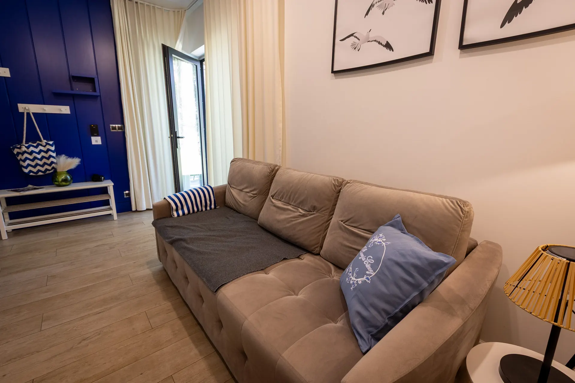 Salon z beżową sofą i otwartymi drzwiami balkonowymi, granatowa ściana wejściowa z wieszakiem — Apartament 3 Poezja Ciszy Dębki